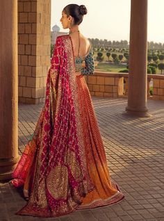 a woman in a red and gold lehenga standing on a brick walkway looking out into the distance