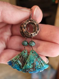 a close up of a person holding a pair of earrings in their hand with shells hanging from them