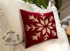 a red and white pillow sitting on top of a bed next to a green plant