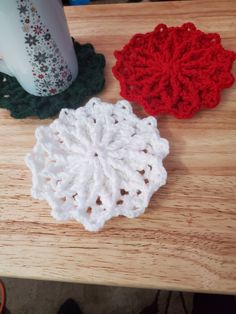 three crocheted coasters sitting on top of a wooden table next to a cup