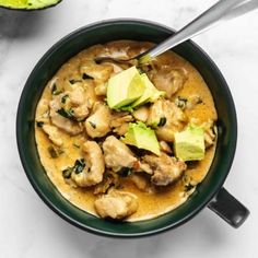 a bowl of chicken and avocado soup on a white table with limes