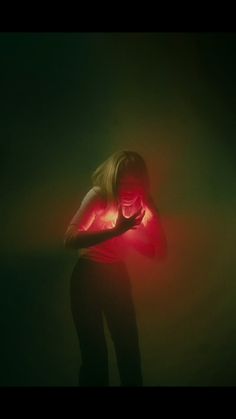 a woman standing in the dark with her hands on her chest