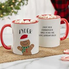 two coffee mugs with marshmallows in the shape of a gingerbread man