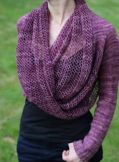 a woman standing in the grass wearing a purple knitted shawl and black dress