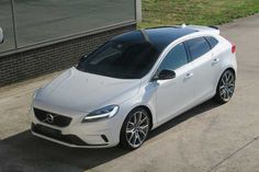 a white volvo car parked in front of a brick building on the side of a road