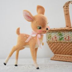 a small stuffed deer standing next to a basket with a pink bow on it's head