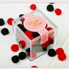 a clear box filled with raspberries on top of a white table next to red and black pom - poms