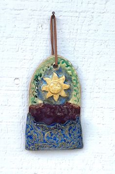 a ceramic sun and moon decoration hanging on a white brick wall with brown leather cord