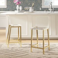 two white bar stools sitting in front of a kitchen counter with flowers on it