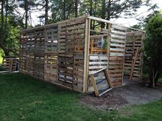 a wooden structure made out of pallets in the grass next to trees and bushes