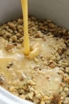 a person pouring orange juice into a white crock pot filled with oatmeal