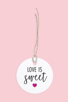 a sign that says love is sweet hanging from a string on a pink background with the words love is sweet