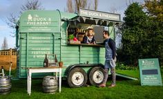 two people standing in the back of a green trailer with food and drinks on it