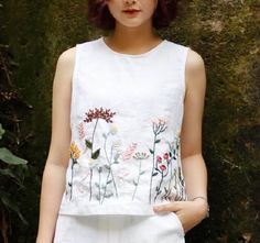 a woman standing in front of a wall wearing white shorts and a top with flowers on it