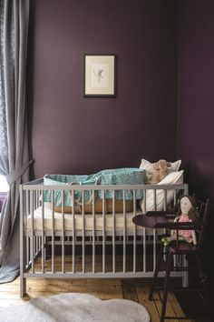 a baby's crib in the corner of a room with purple walls and curtains