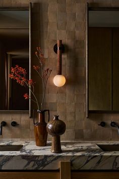 two vases with flowers in them sit on a marble countertop next to mirrors