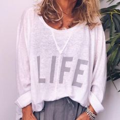 a woman standing in front of a plant wearing a white shirt with the word life on it