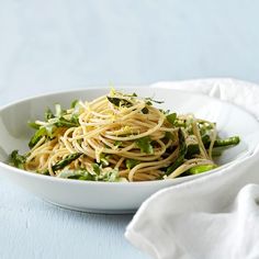 a white bowl filled with pasta and asparagus on top of a blue table