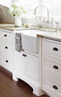 a white kitchen sink sitting under a window next to a counter top with flowers on it