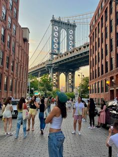 many people are walking on the sidewalk in front of some tall buildings and a bridge