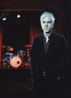 a man with white hair standing in front of a drum set and drums behind him