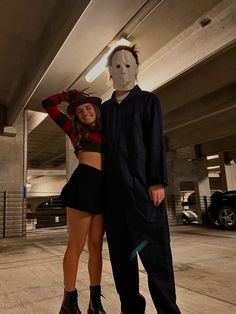 two people in costumes standing next to each other near a parking garage with one person wearing a mask