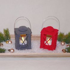 three small crocheted lanterns sitting on top of snow next to evergreen branches and pine cones