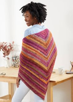 a woman wearing a crocheted shawl standing in front of a table