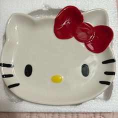 a hello kitty dish with red bows on it's head and eyes, sitting on a white towel