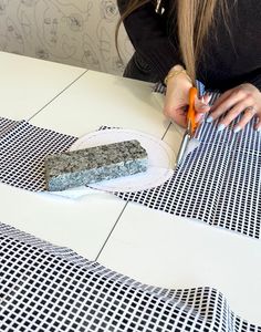 a woman cutting into a piece of cake on top of a white table with black and white checkered cloth