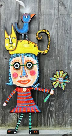 a colorful paper doll is hanging on a wooden fence with a bird perched on it's head