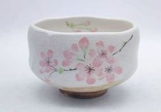 a small white bowl with pink flowers painted on it's sides and wooden base