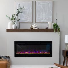 an electric fireplace in a living room with two pictures on the wall above it and a potted plant