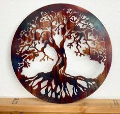 a metal tree with many leaves on it sitting on top of a wooden shelf next to a white wall