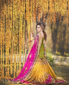 a woman in a yellow and pink dress standing under a tree with flowers hanging from it