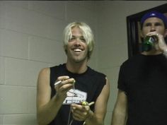 two men standing next to each other in a bathroom holding game controllers and drinking beer