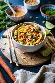 a bowl filled with noodles and vegetables on top of a cutting board next to chopsticks