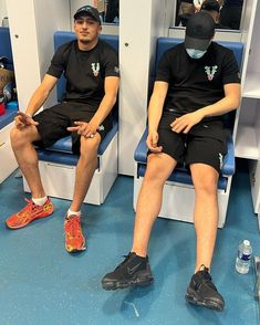 two men in black shirts and shorts sitting next to each other on blue flooring