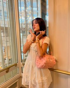 a woman standing in front of a window talking on a cell phone and holding a purse