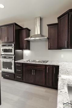 an empty kitchen with granite counter tops and dark wood cabinets, along with stainless steel appliances