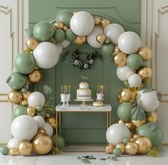 a table topped with cake and balloons in front of a green door covered in greenery