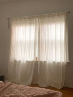 a bed sitting under a window next to a white curtained wall and wooden floor