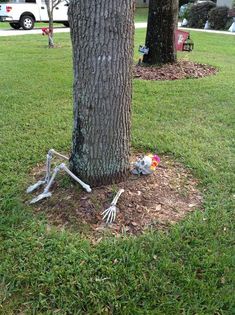 a skeleton sitting under a tree in the middle of a yard next to a halloween decoration