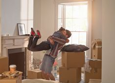 a man and woman are hugging in the middle of moving boxes into their new home