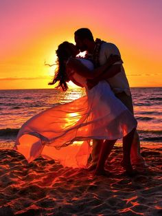 a bride and groom kissing on the beach at sunset