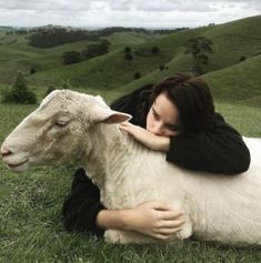 a woman laying on the ground with a sheep in her lap and looking at the camera