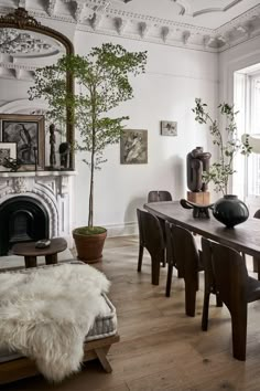 a dining room table with chairs and a bench in front of a fire place that has a potted plant on it