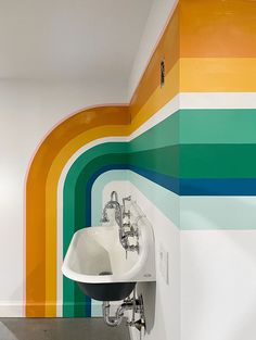 a white sink sitting under a rainbow painted wall