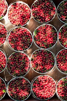 buckets filled with cherries sitting on top of a wooden table next to each other