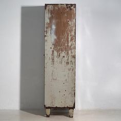 an old wooden cabinet sitting against a white wall with peeling paint on the door and bottom